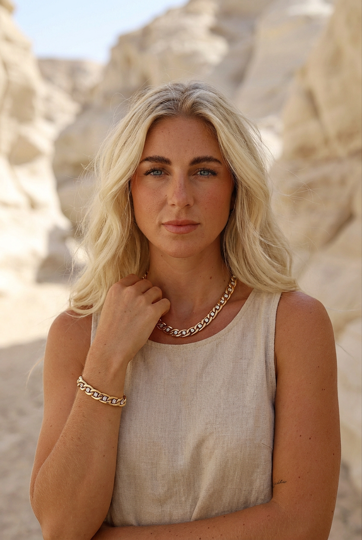 Woman with blonde hair and a chunky gold chain necklace standing in front of rocky terrain
