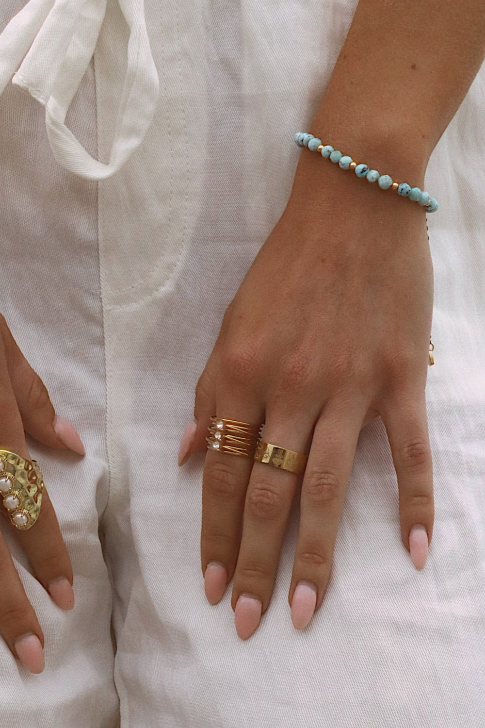Close-up of hands wearing gold rings on white pants